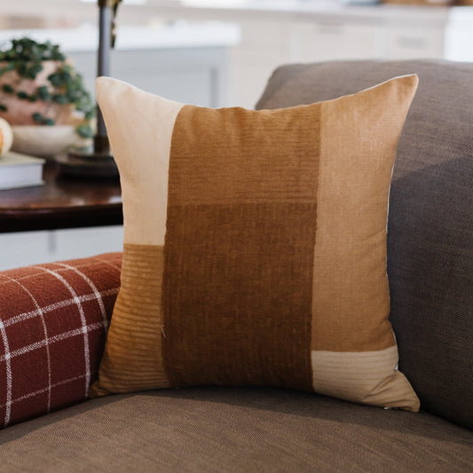 Tan and brown color-block pillow with textured fabric panels displayed on gray sofa.