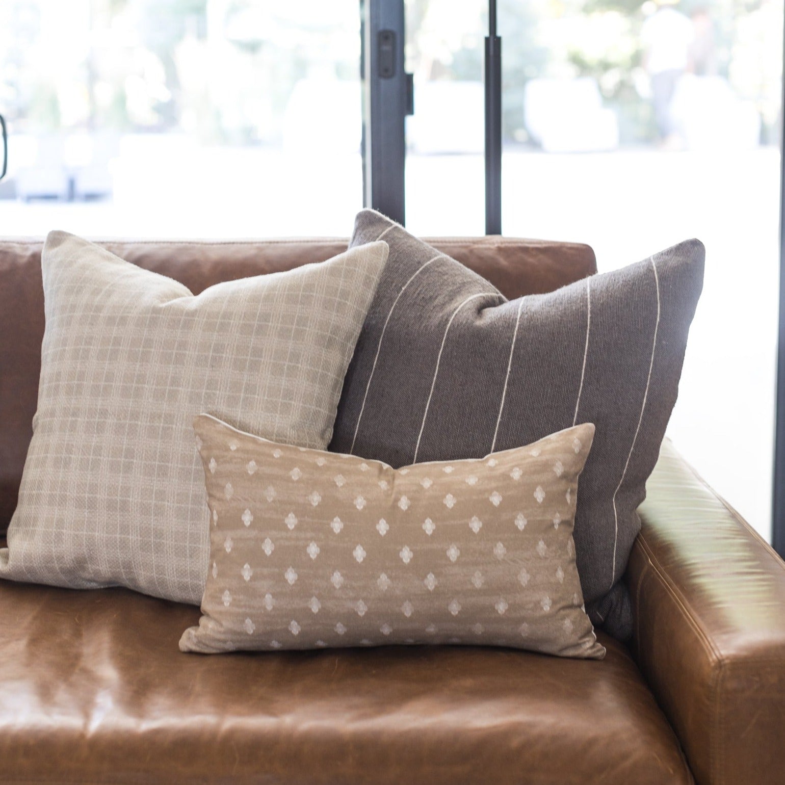Taupe throw pillow with white geometric diamond pattern on brown leather sofa.