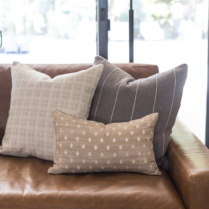Taupe throw pillow with white geometric diamond pattern on brown leather sofa.