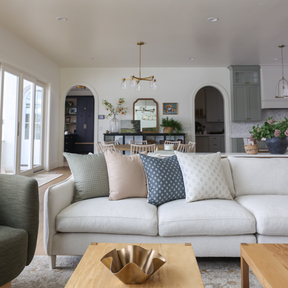 Four decorative pillows in green check, blush, blue with white dots, and cream patterns displayed on a cream sofa.