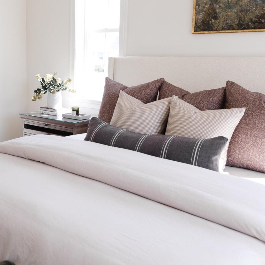 Charcoal lumbar pillow with white stripes displayed on a bed with coordinating patterned pillows.