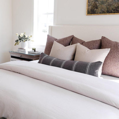 Charcoal lumbar pillow with white stripes displayed on a bed with coordinating patterned pillows.
