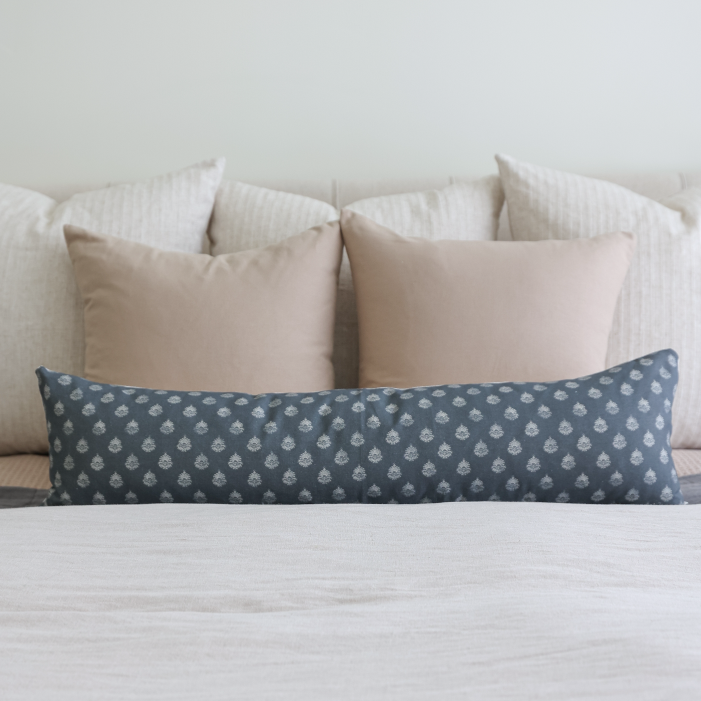 Tan solid pillow cover displayed on bed with white striped and patterned blue pillows.