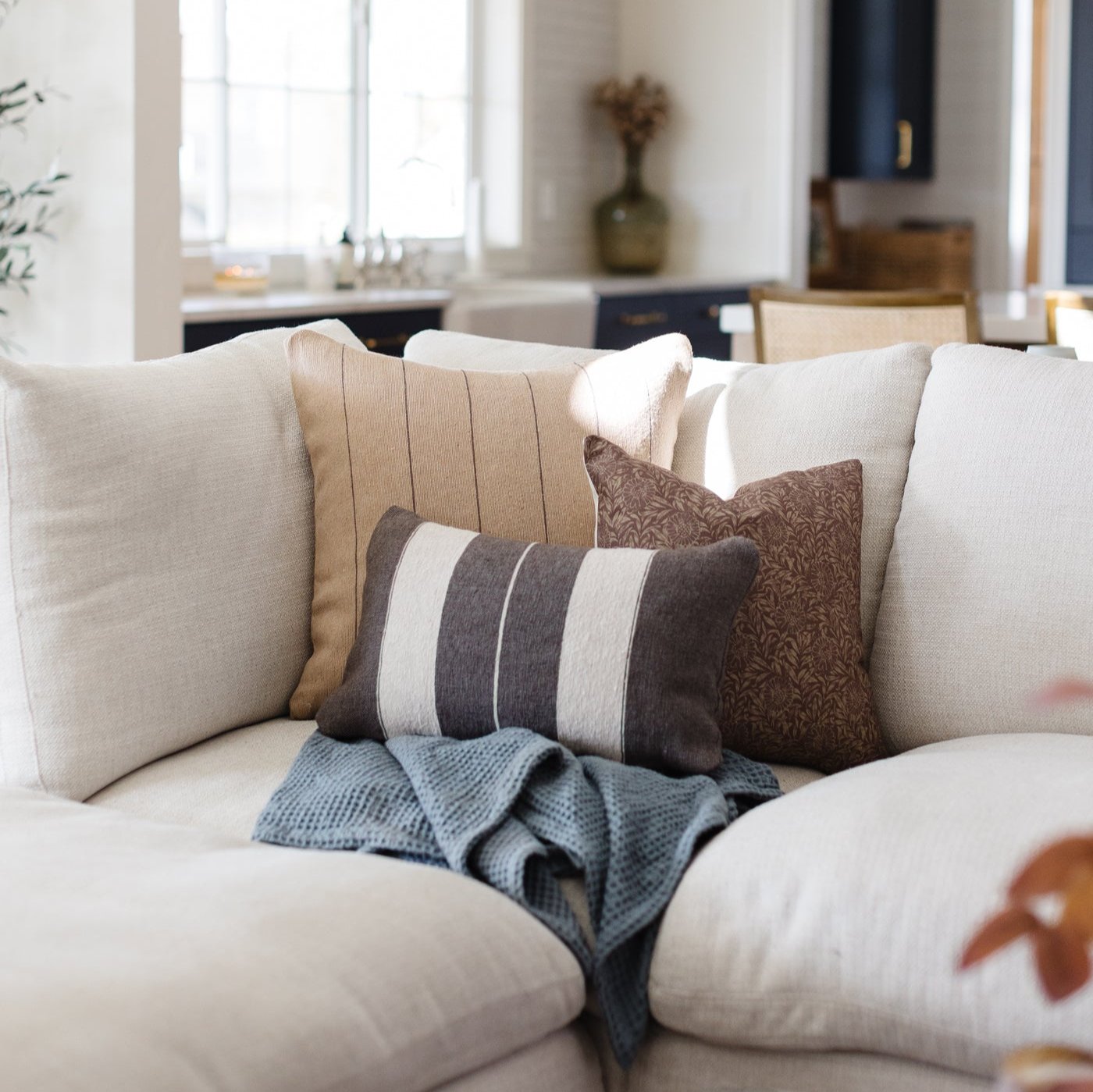 Cream upholstered sofa with decorative pillows in neutral and brown tones, styled in a bright living room setting.