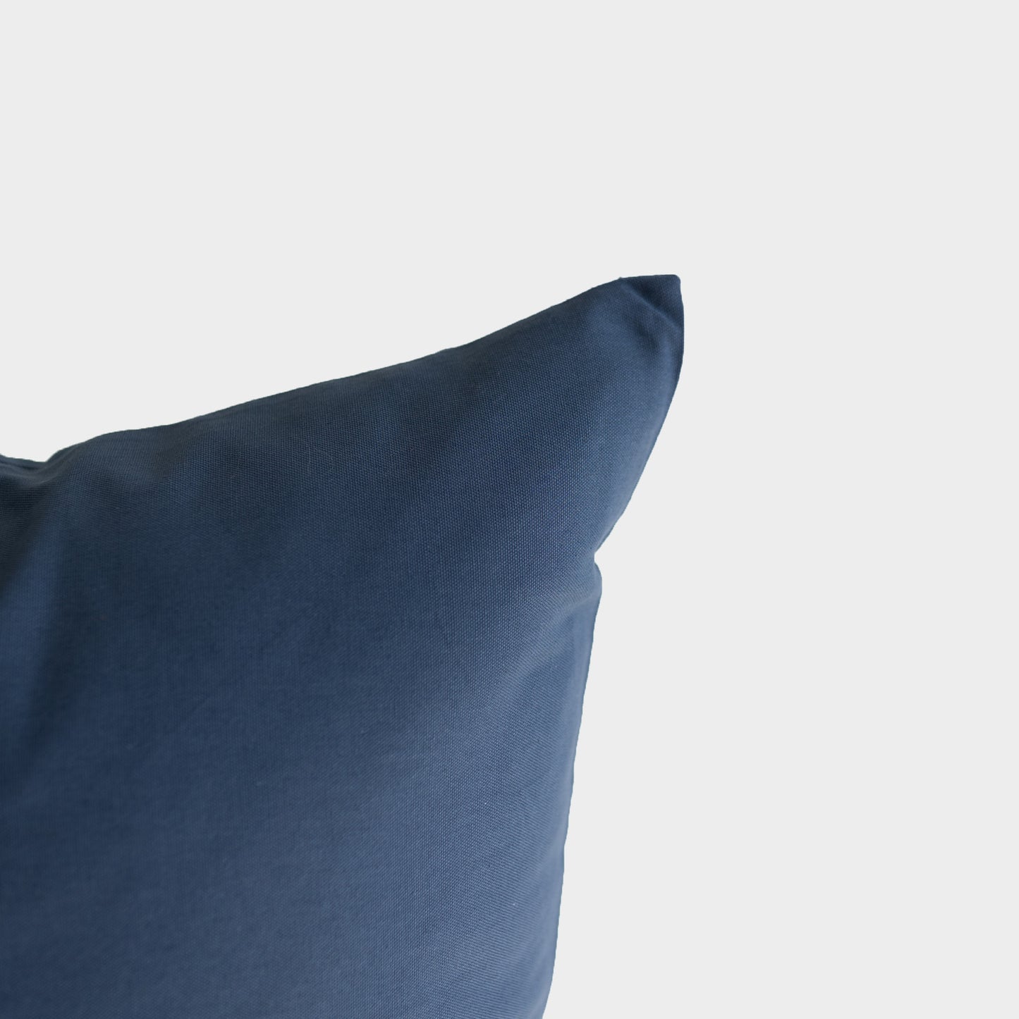 Navy blue pillow with soft fabric texture and rounded corner visible against white background.