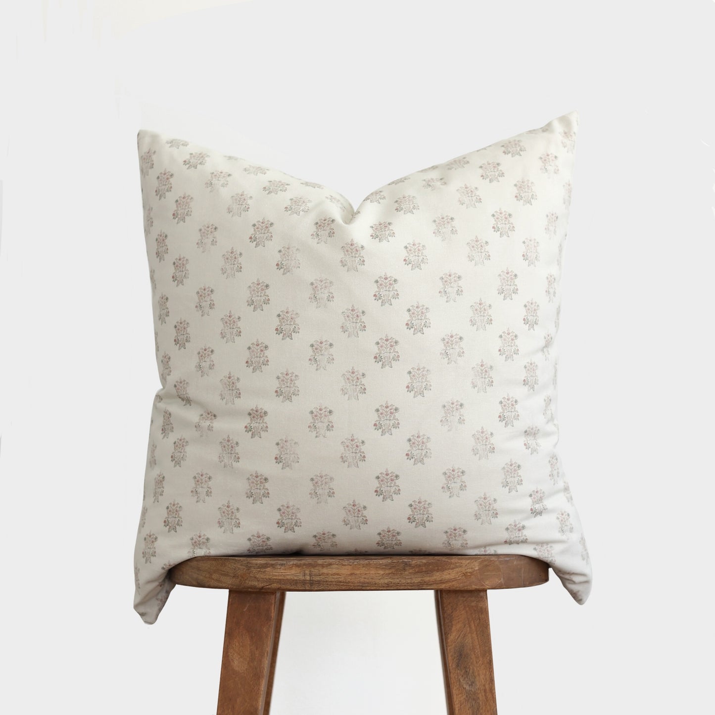 Cream pillow with mauve floral pattern displayed on wooden stool.