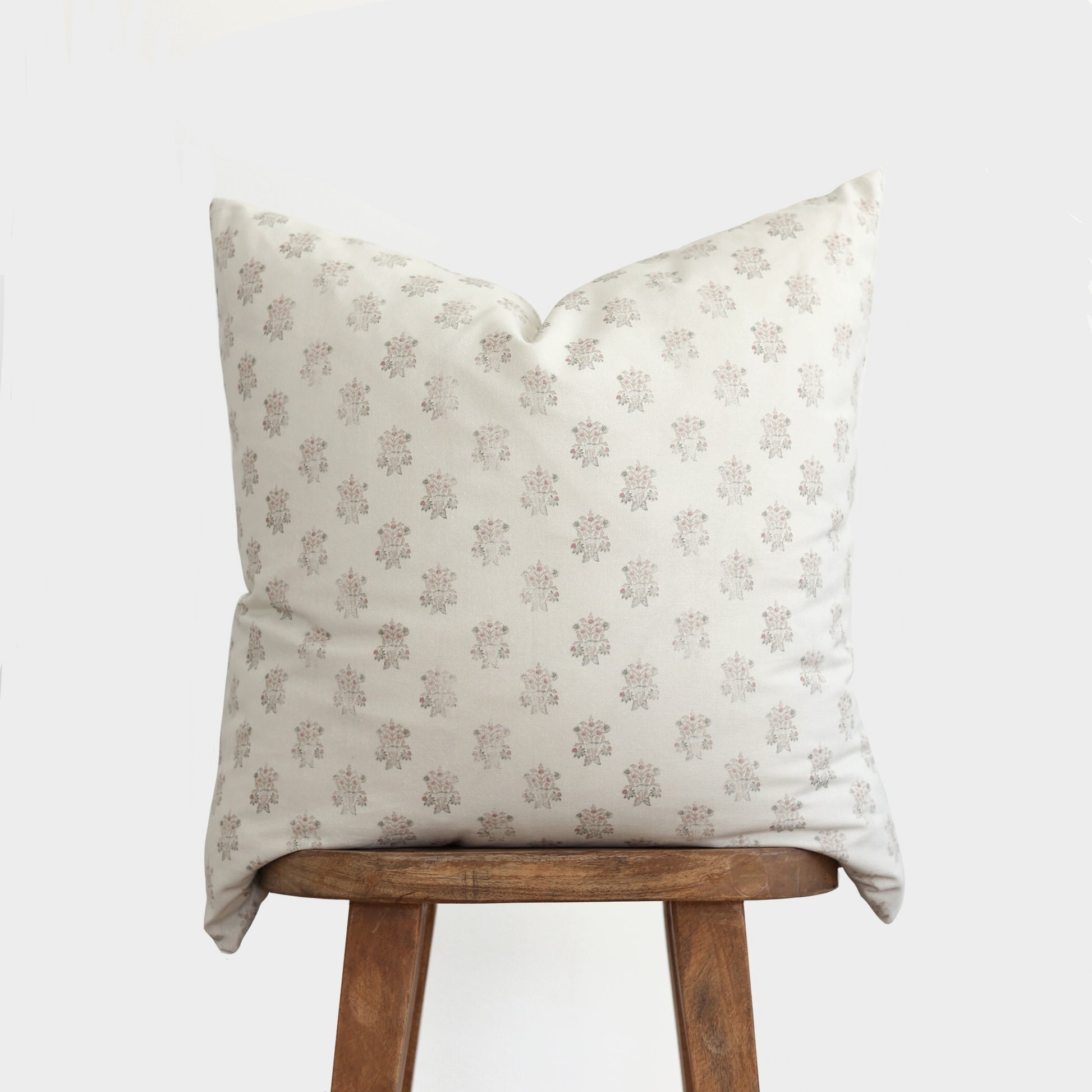 Cream pillow with mauve floral pattern displayed on wooden stool.