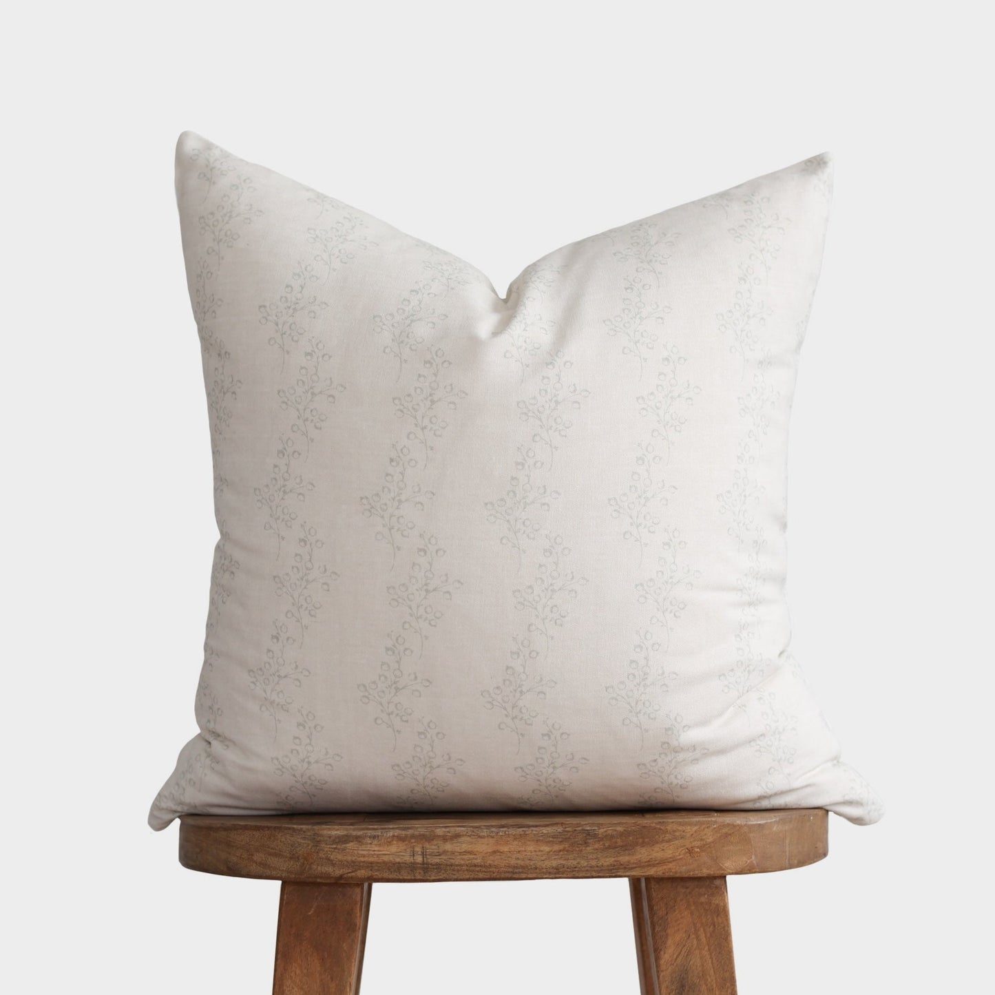 Cream pillow with delicate repeating floral pattern, displayed on wooden stool.