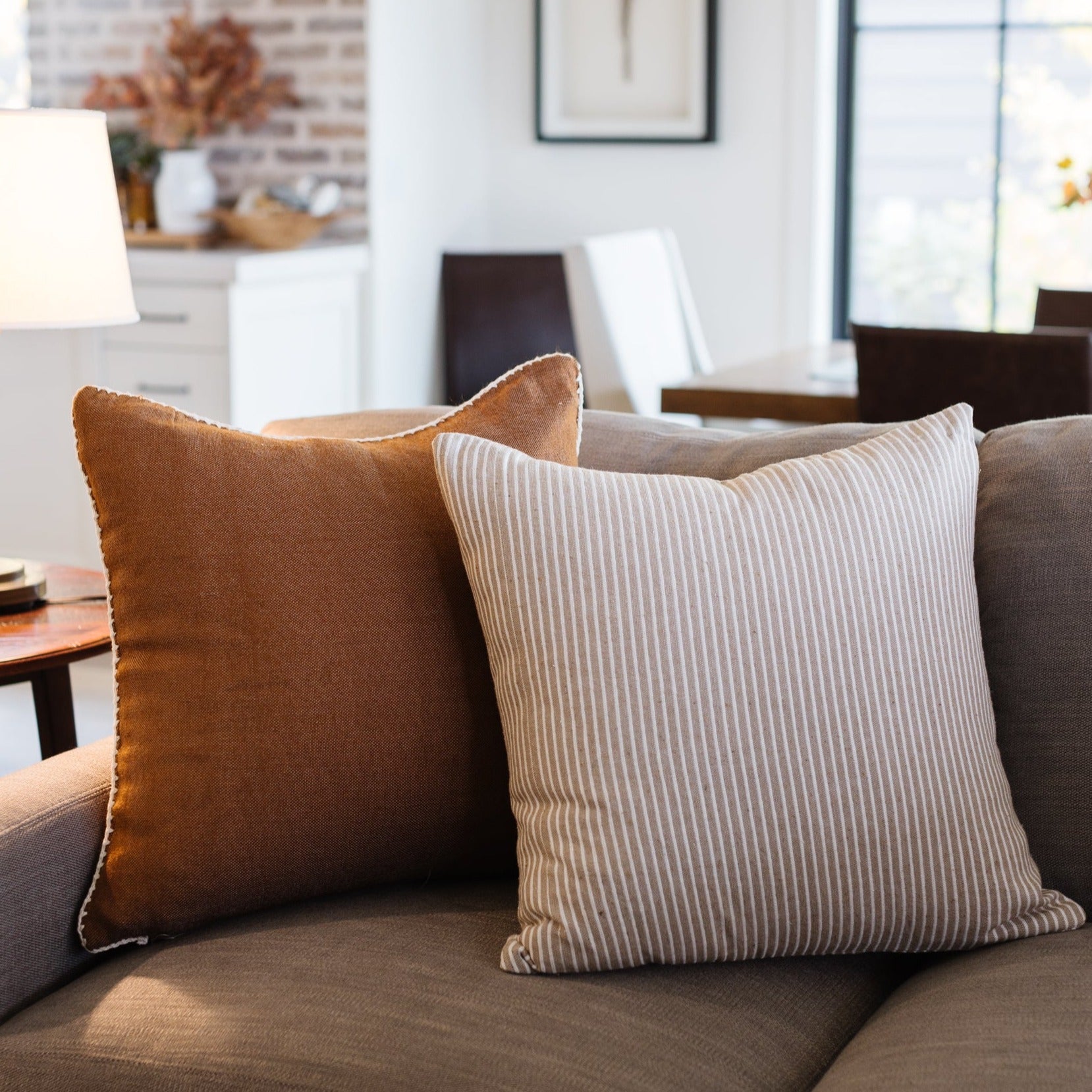 Rust-brown and beige striped throw pillows arranged on a gray upholstered sofa in a modern living room.