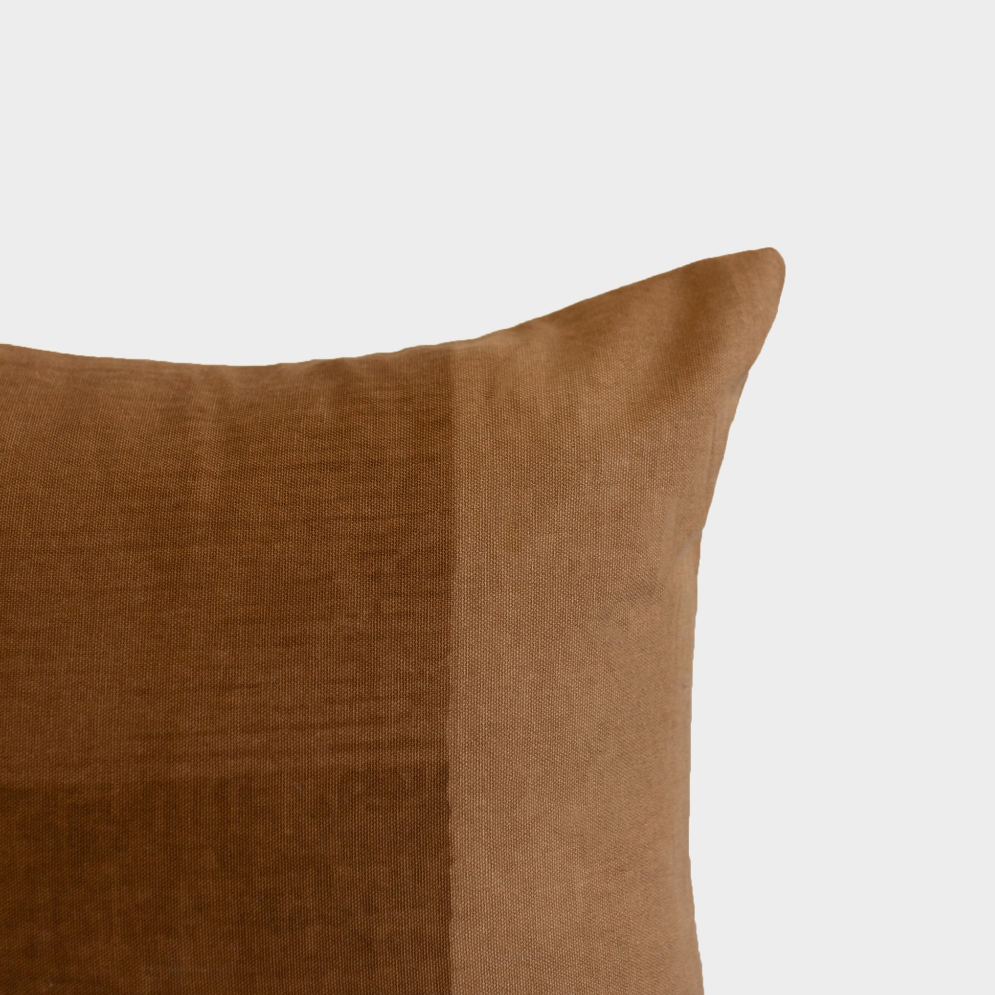 Brown woven pillow with a subtle texture and curved corner detail against a light background.