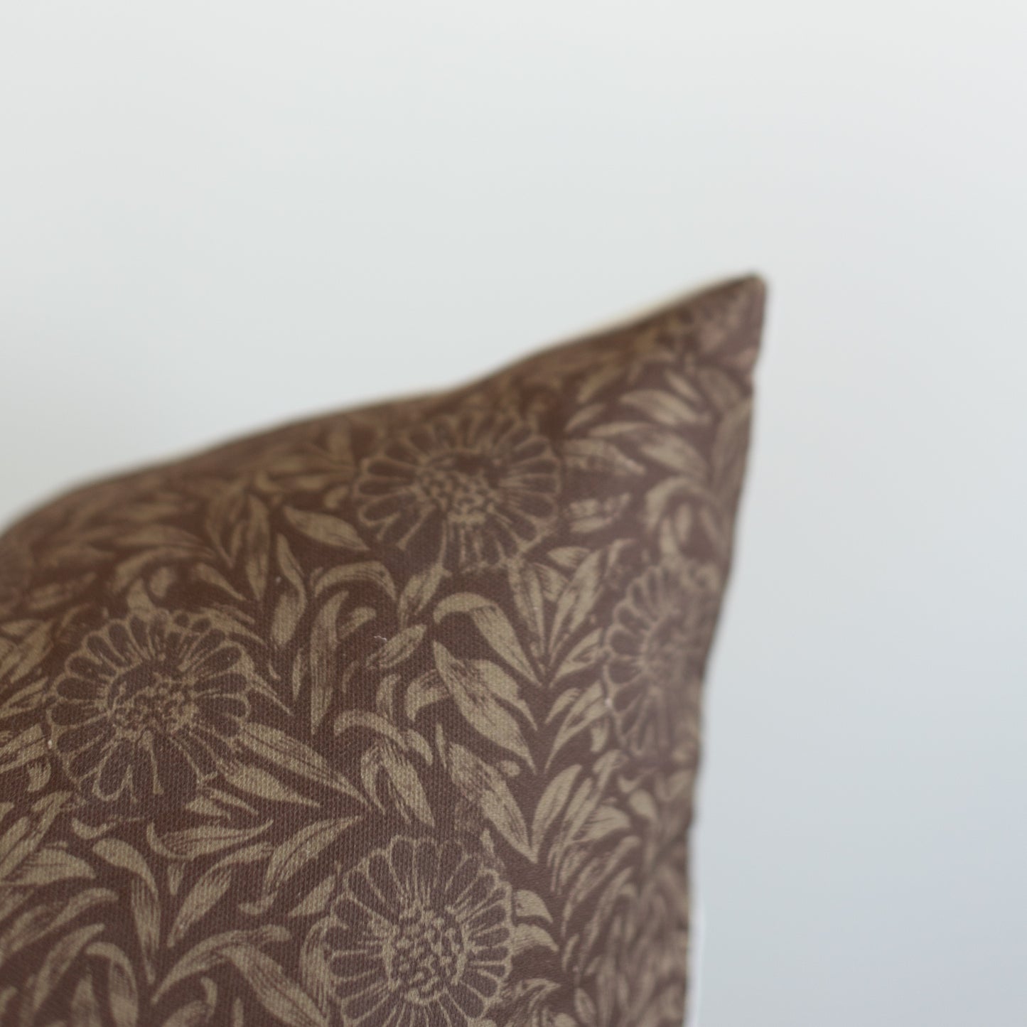 Brown and beige floral patterned pillow corner with botanical sunflower and leaf design.
