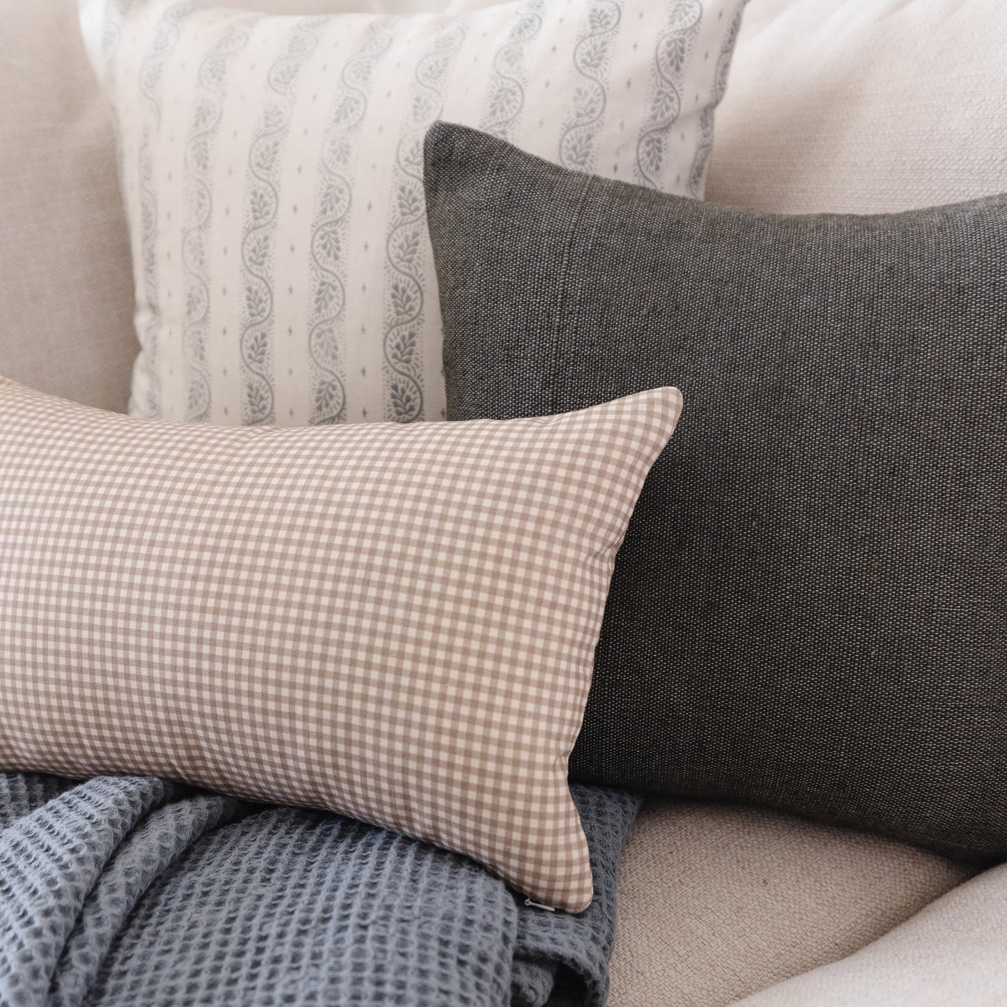 Tan and white gingham lumbar pillow displayed with coordinating patterned pillows on a neutral sofa.