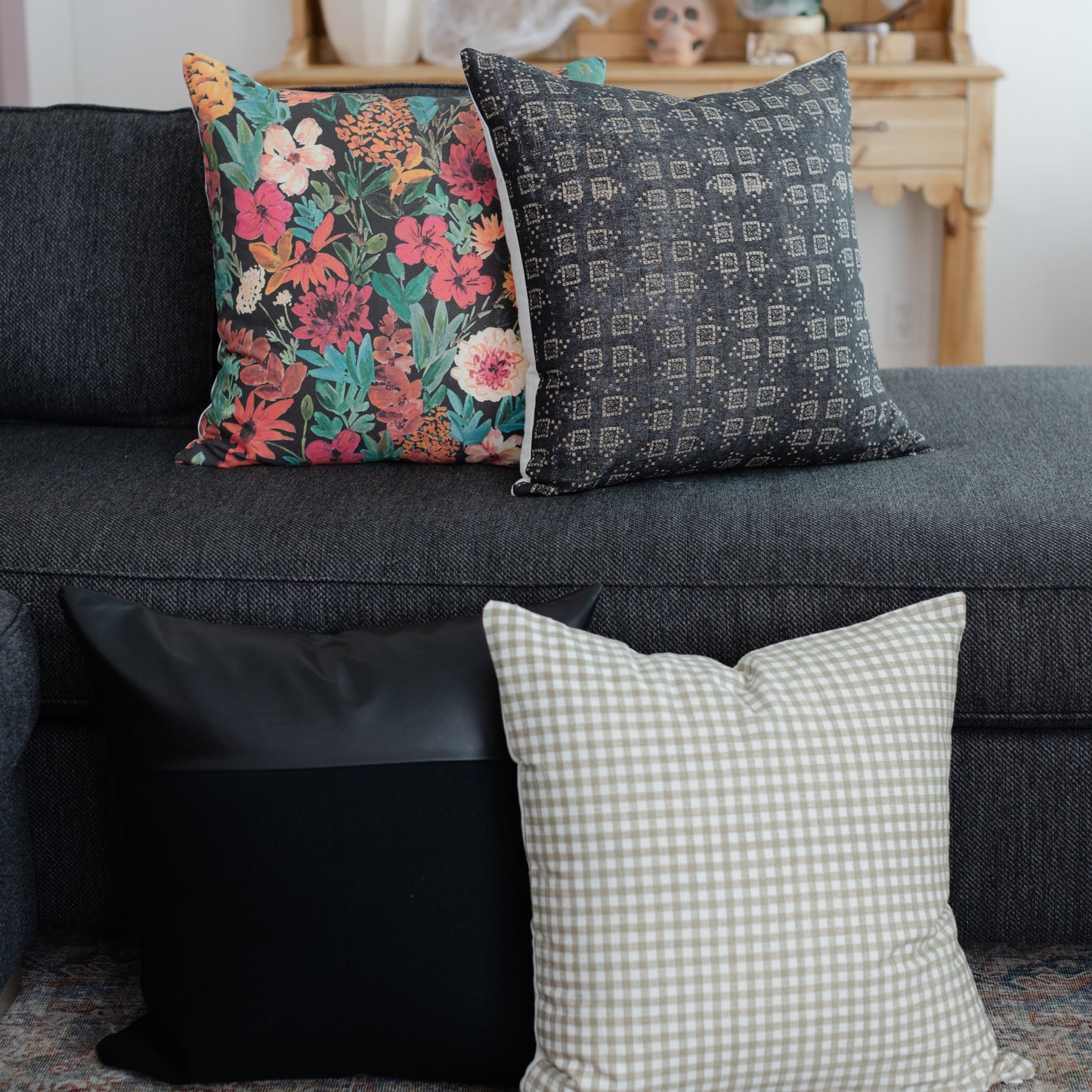 Three decorative throw pillows displayed on a gray sofa: floral patterned, geometric patterned, and gingham check.