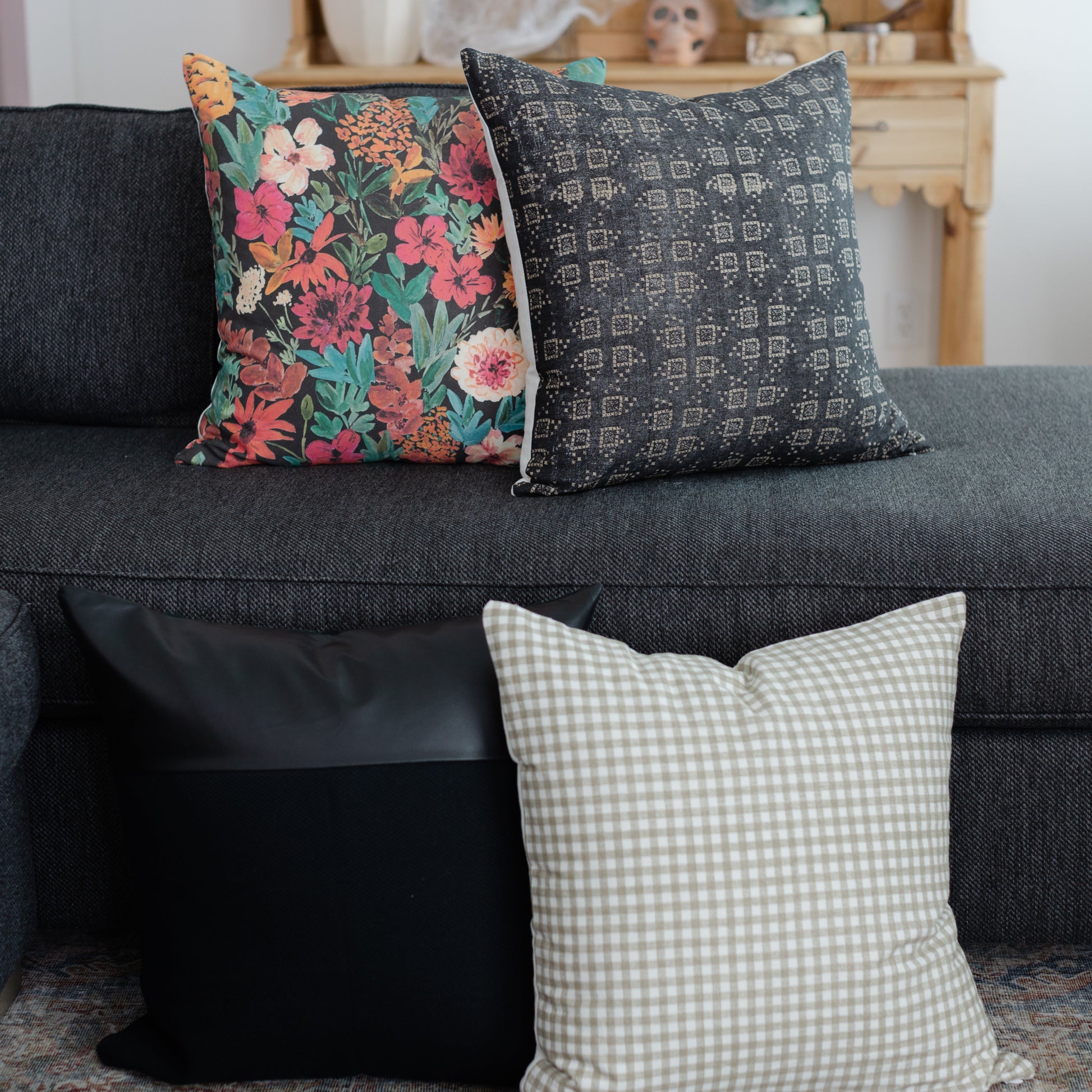 Three decorative throw pillows displayed on a gray sofa: floral patterned, geometric patterned, and gingham check.