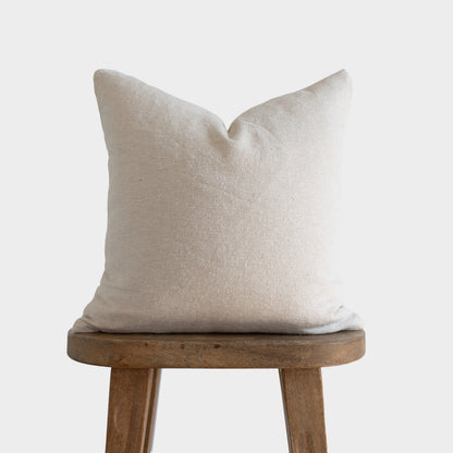 Off-white boucle pillow with textured fabric displayed on wooden stool.