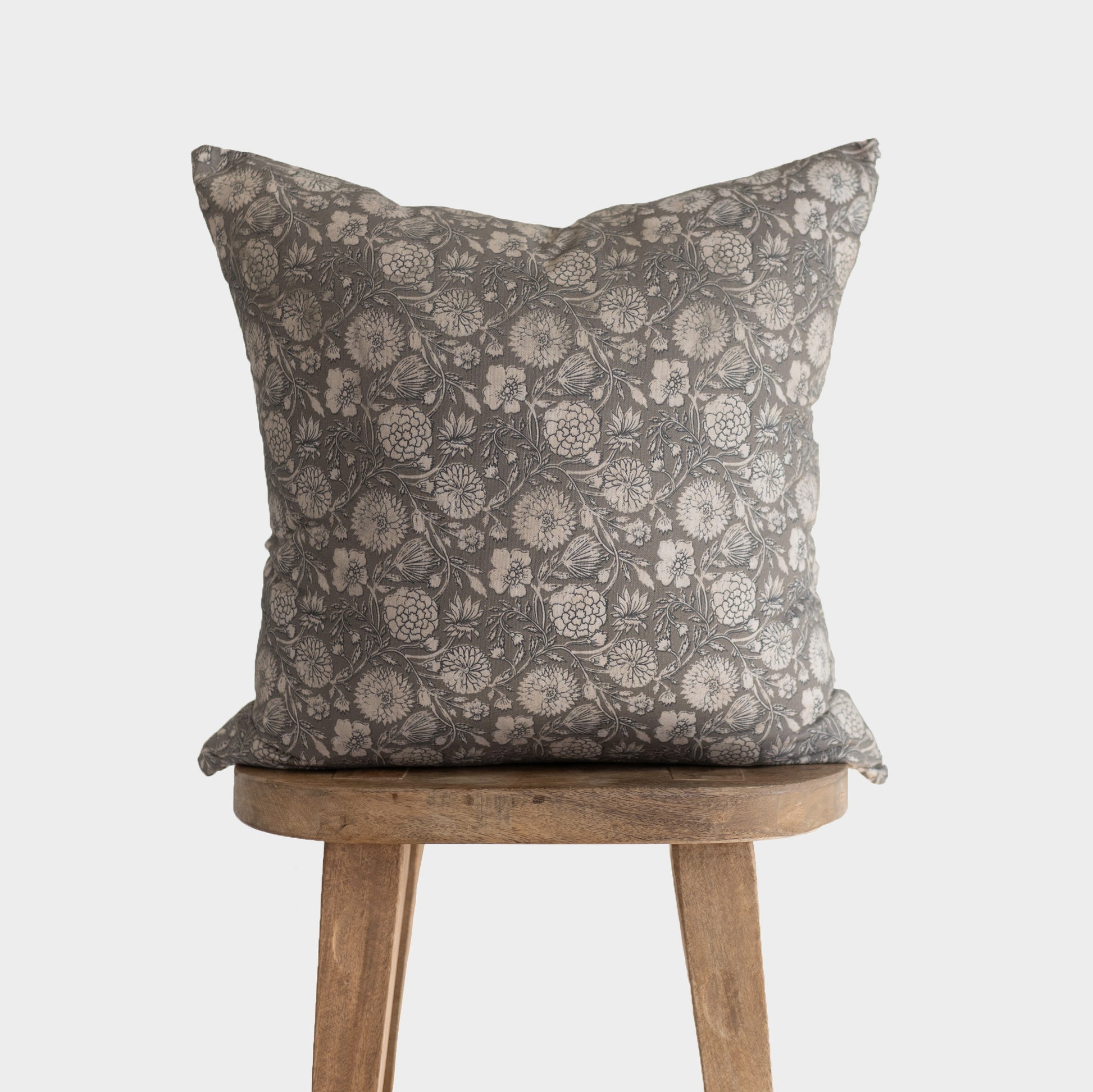 Gray floral patterned pillow with botanical print displayed on wooden stool.
