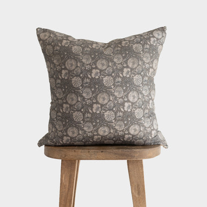 Gray floral patterned pillow with botanical print displayed on wooden stool.