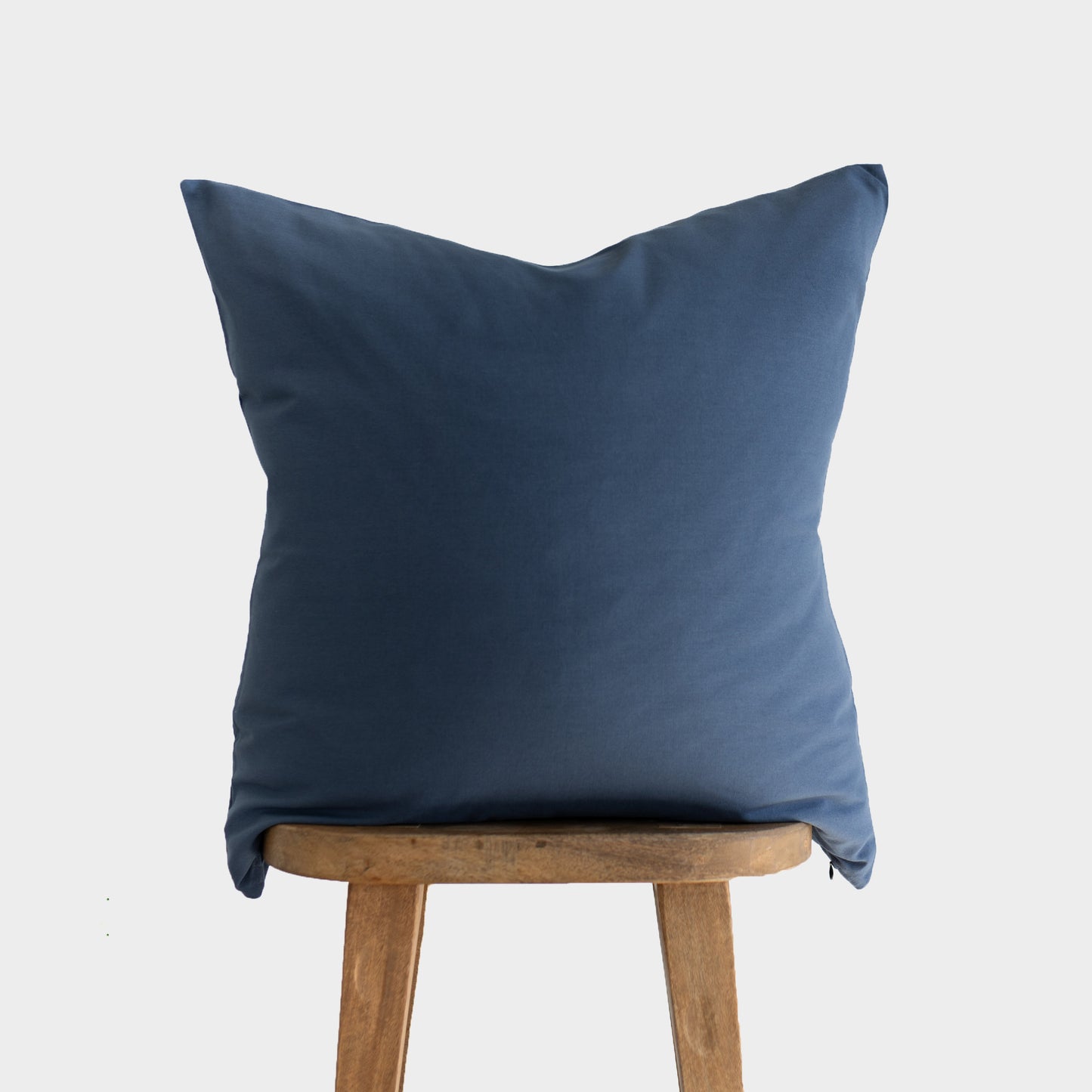Navy blue throw pillow with folded corners displayed on wooden stool.