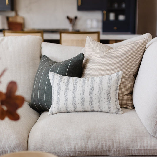 White and tan small gingham check lumbar pillow displayed on a cream sofa with coordinating pillows.