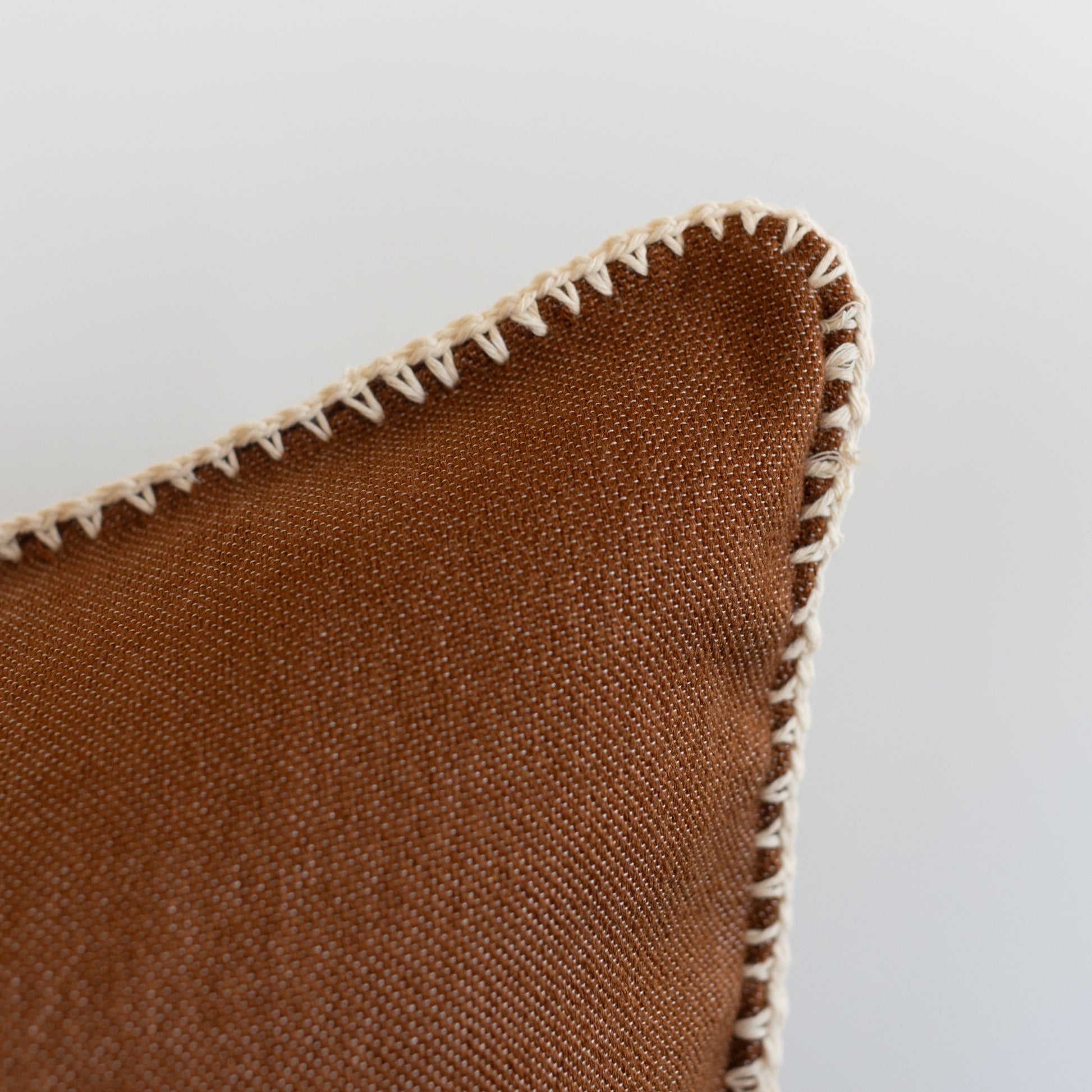 Spice-colored woven pillow with cream scalloped edge trim and textured fabric surface.