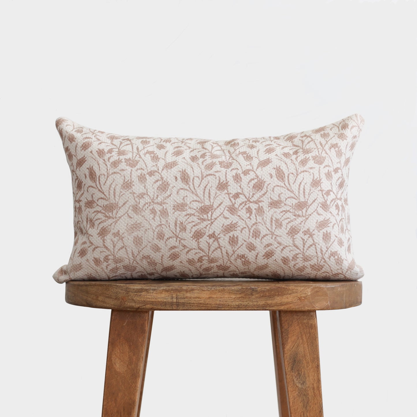 Rectangular pillow with cream and taupe leaf pattern, displayed on wooden stool.