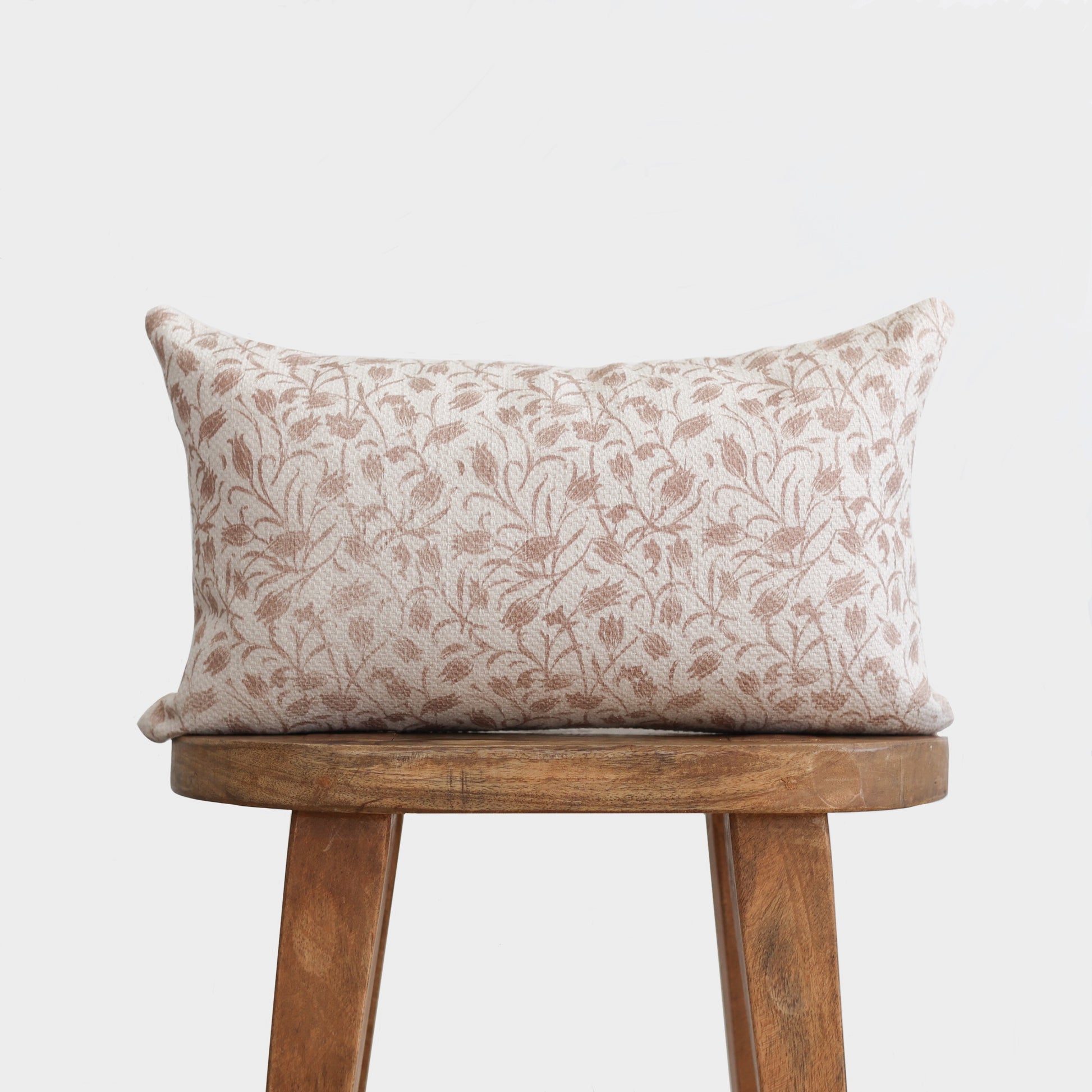 Rectangular pillow with cream and taupe leaf pattern, displayed on wooden stool.