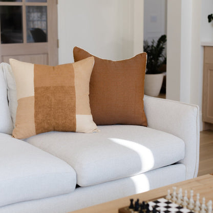 Two throw pillows on a white sofa: one with tan and cream vertical stripes, one solid tan.