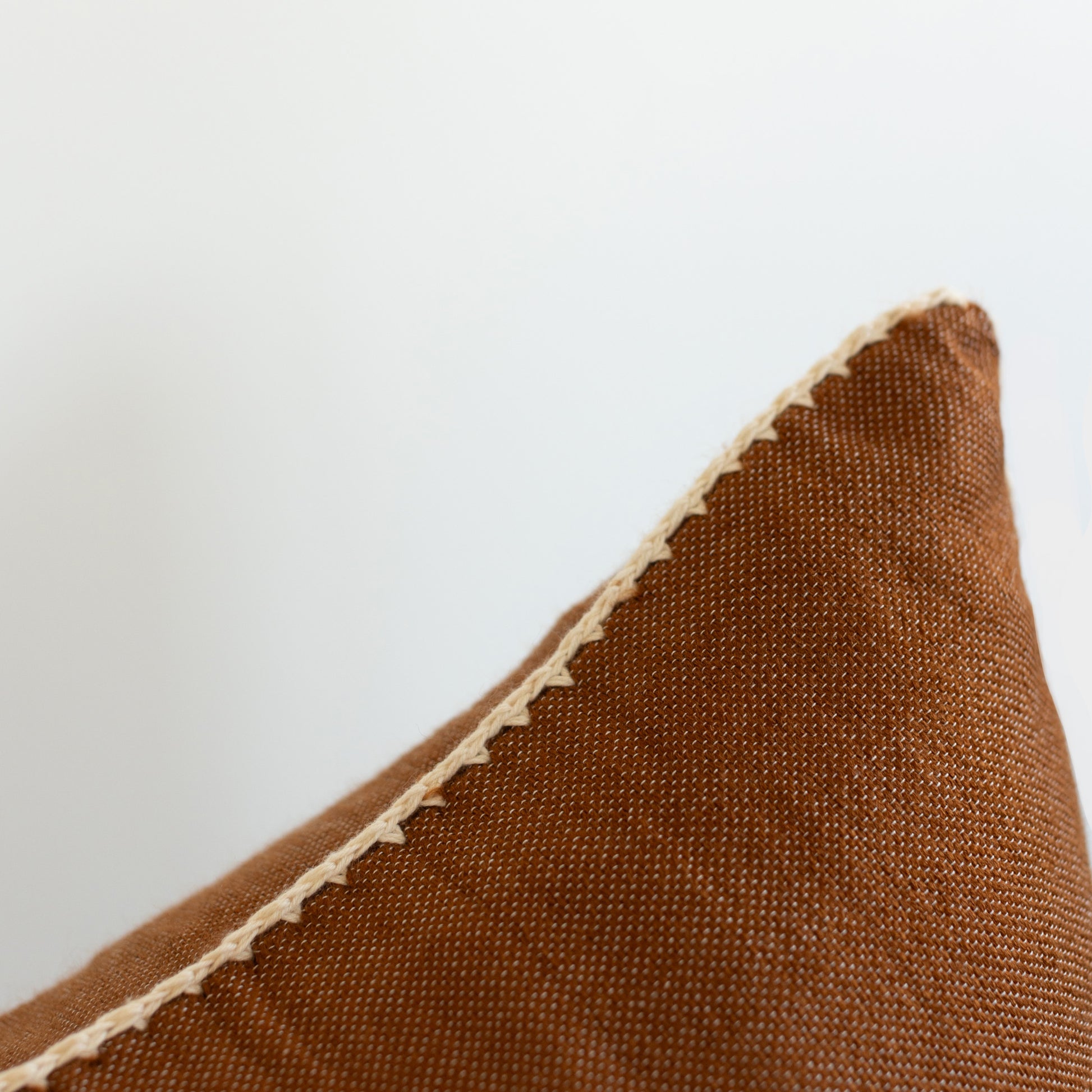 Brown woven pillow with cream binding along the edge against a light background.