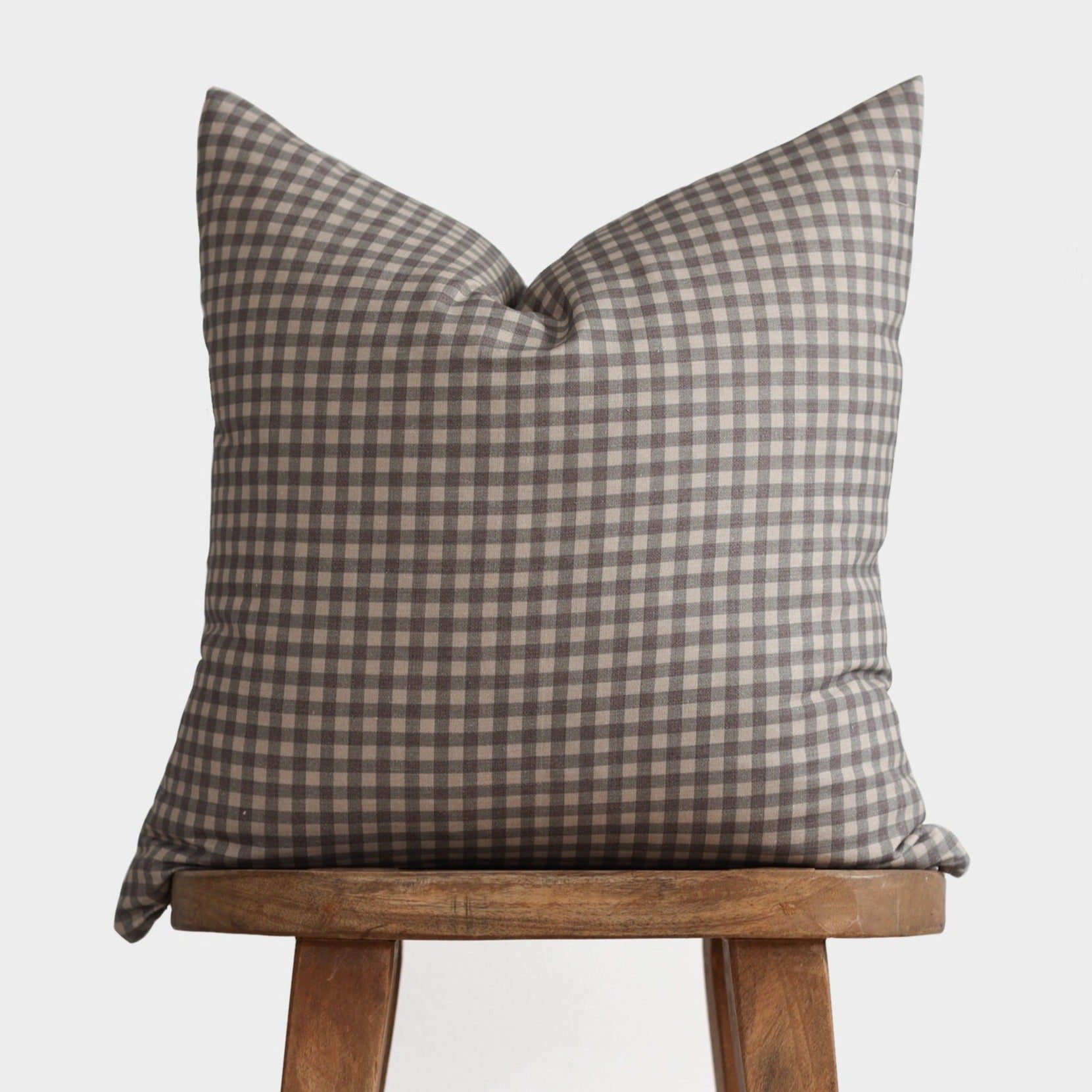 Brown and cream gingham patterned pillow cover displayed on a wooden stool.