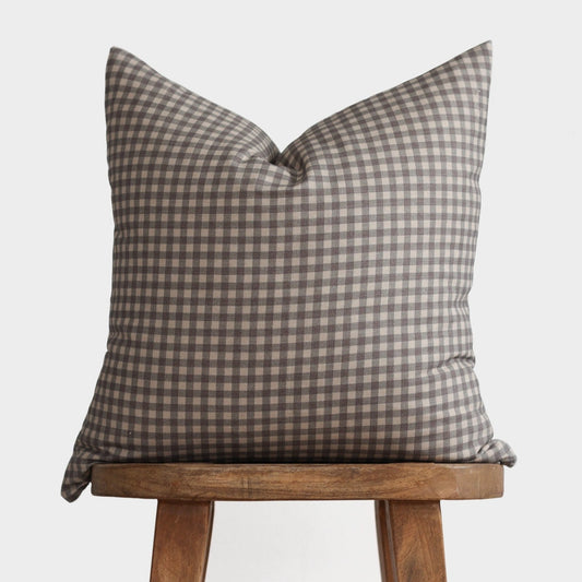 Brown and cream gingham patterned pillow cover displayed on a wooden stool.