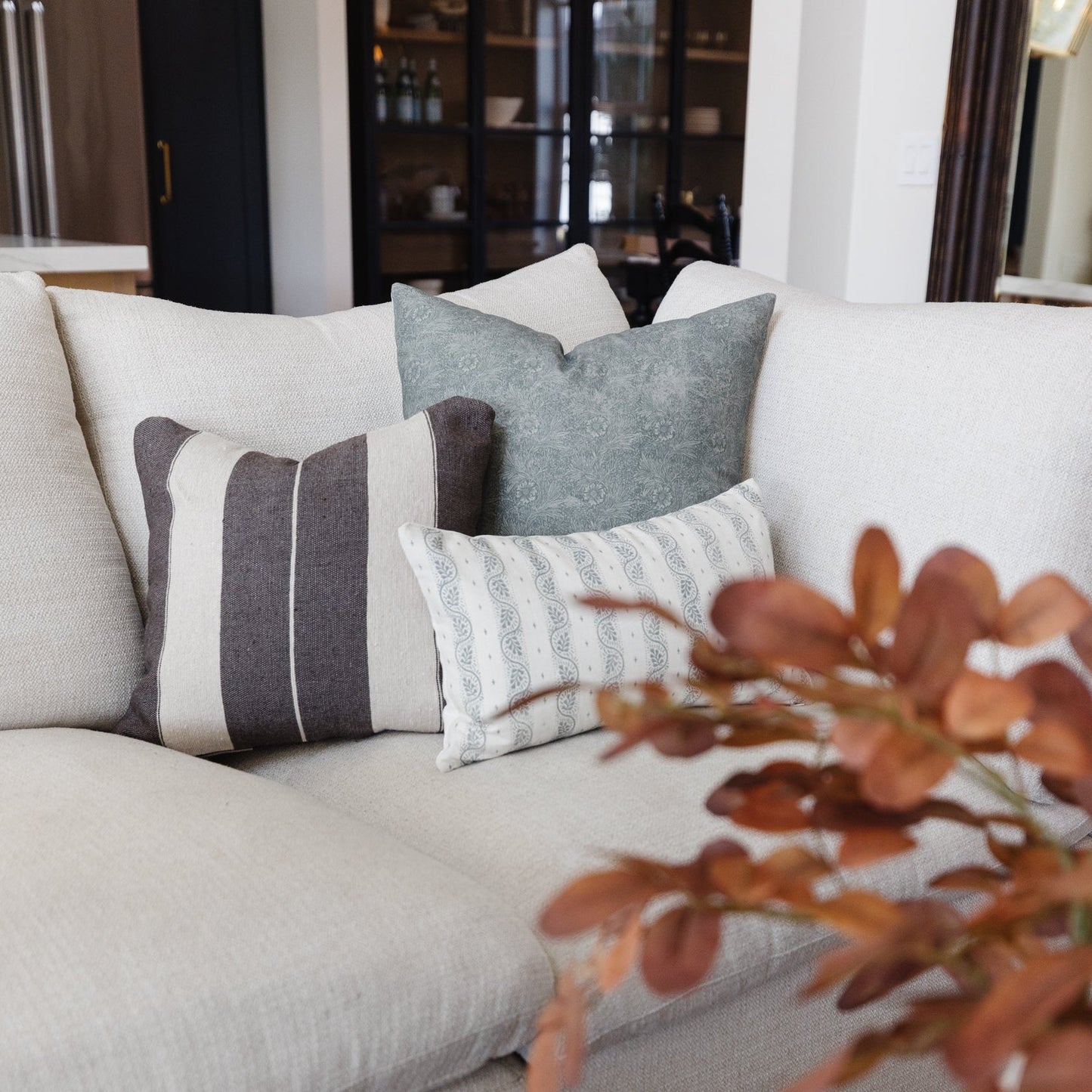 Lumbar pillow with charcoal stripes and white trim on cream sofa, styled with solid gray and patterned pillows.