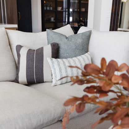Cream, gray, and patterned throw pillows arranged on a beige sofa with dried branches in foreground.