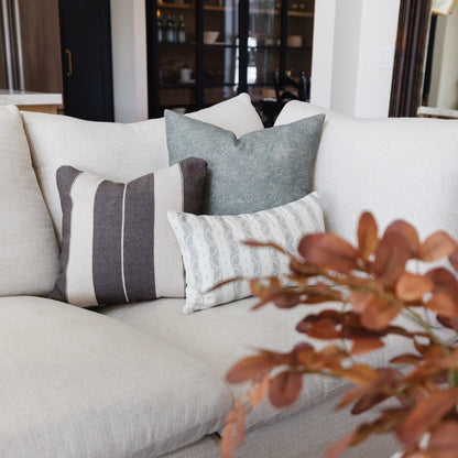 Multiple decorative pillows in neutral and patterned fabrics arranged on a cream-colored sofa.