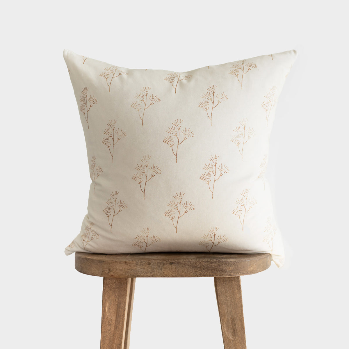 Cream pillow with tan thistle plant pattern, displayed on wooden stool.