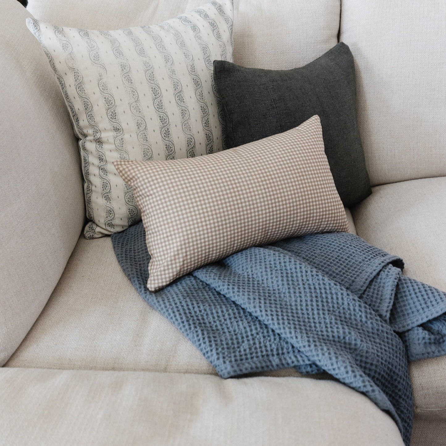 Storm blue waffle-textured blanket draped on a beige sofa with coordinating pillows.