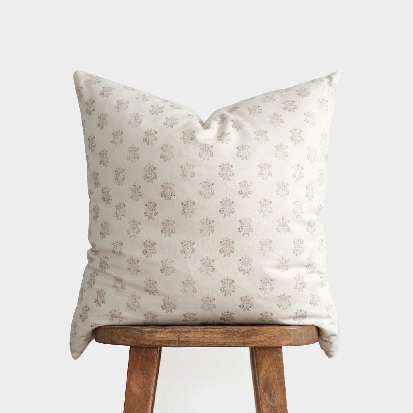 Cream linen pillow with repeating taupe floral motifs, displayed on wooden stool.