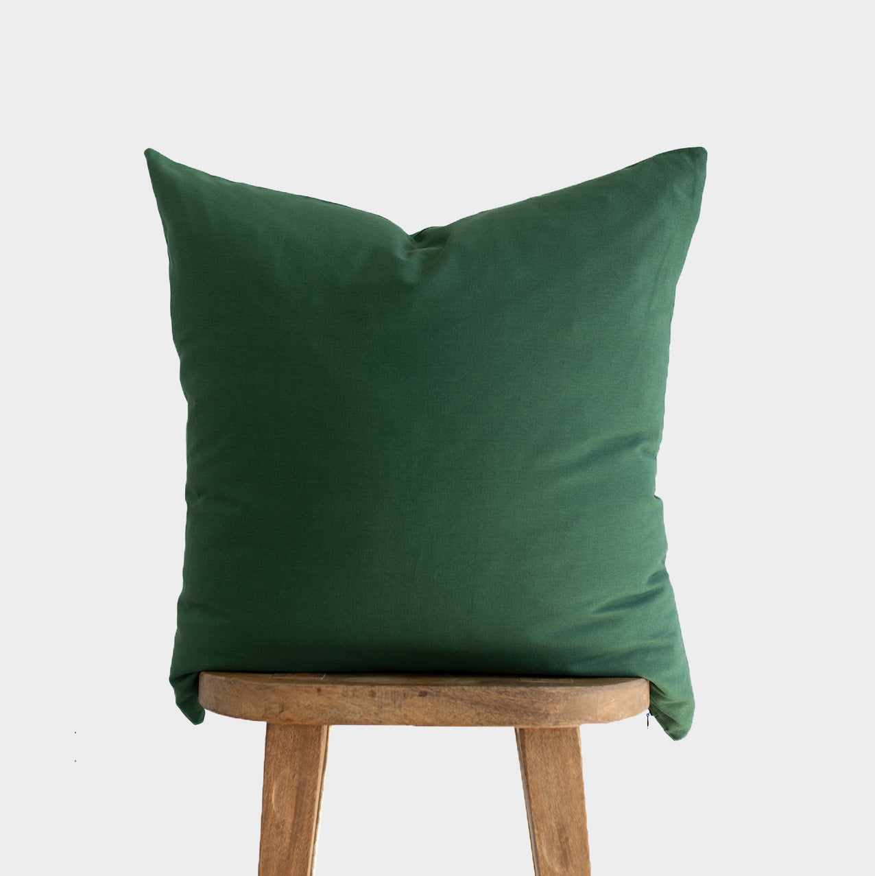 Dark green pillow cover displayed on wooden stool against neutral background.