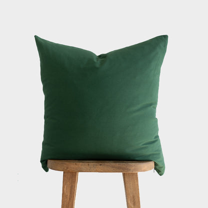Dark green pillow cover displayed on wooden stool against neutral background.