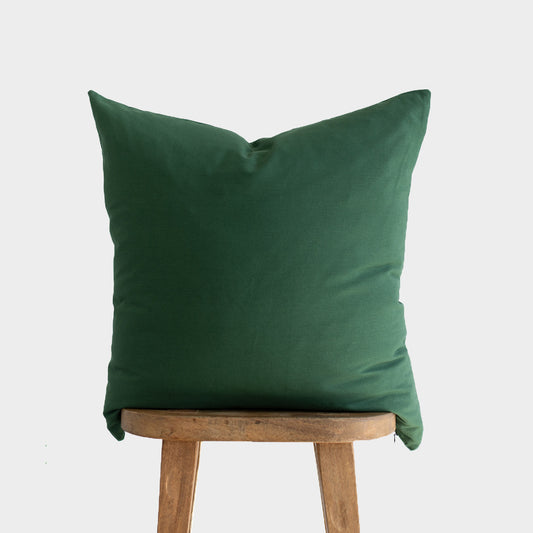 Dark green pillow cover displayed on wooden stool against neutral background.