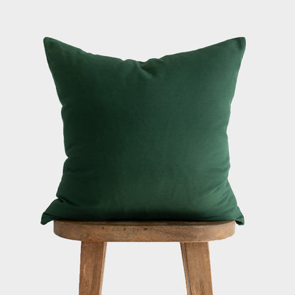 Dark green pillow with textured fabric resting on wooden stool with three legs.