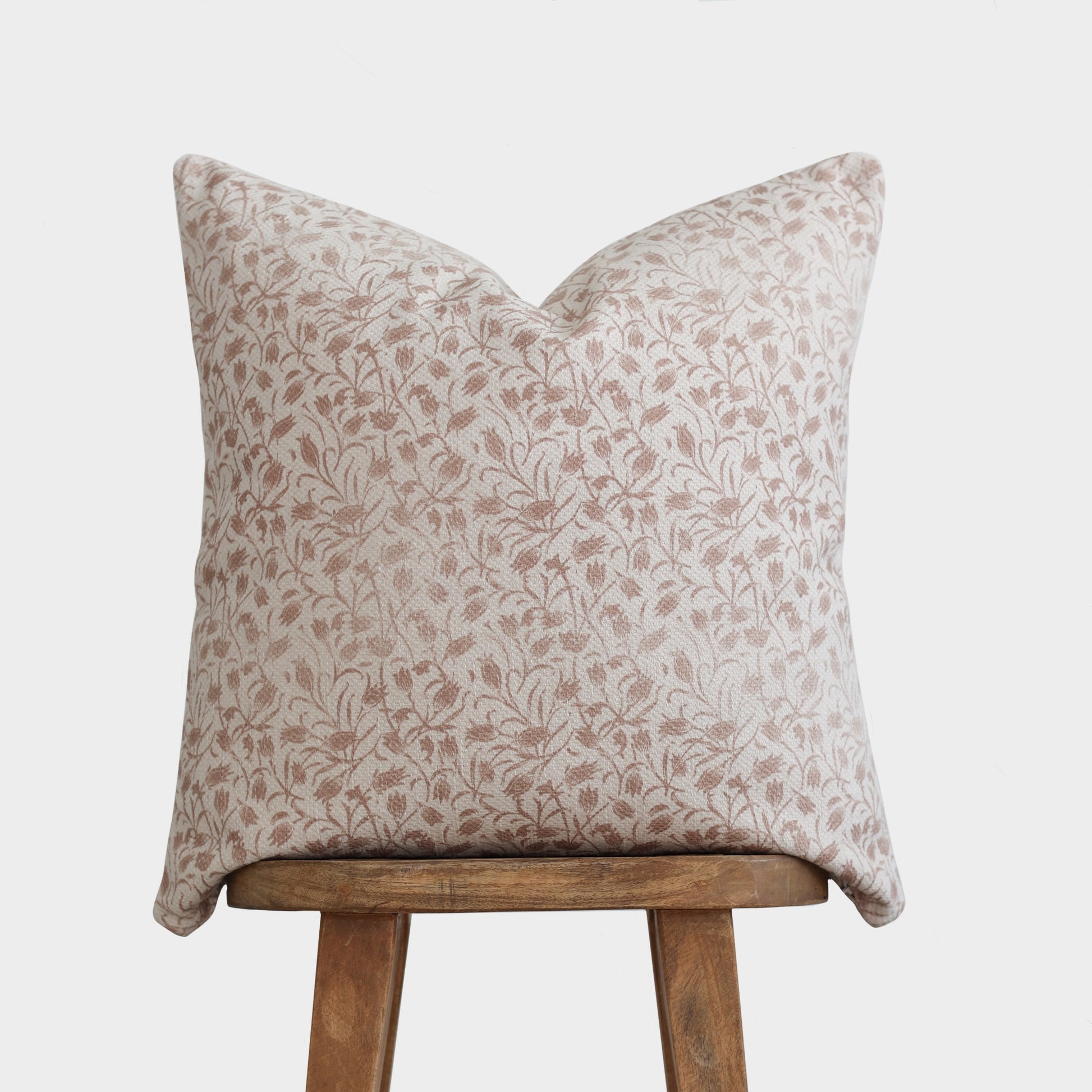 Beige and cream floral patterned pillow cover with thick weave texture displayed on wooden stool.