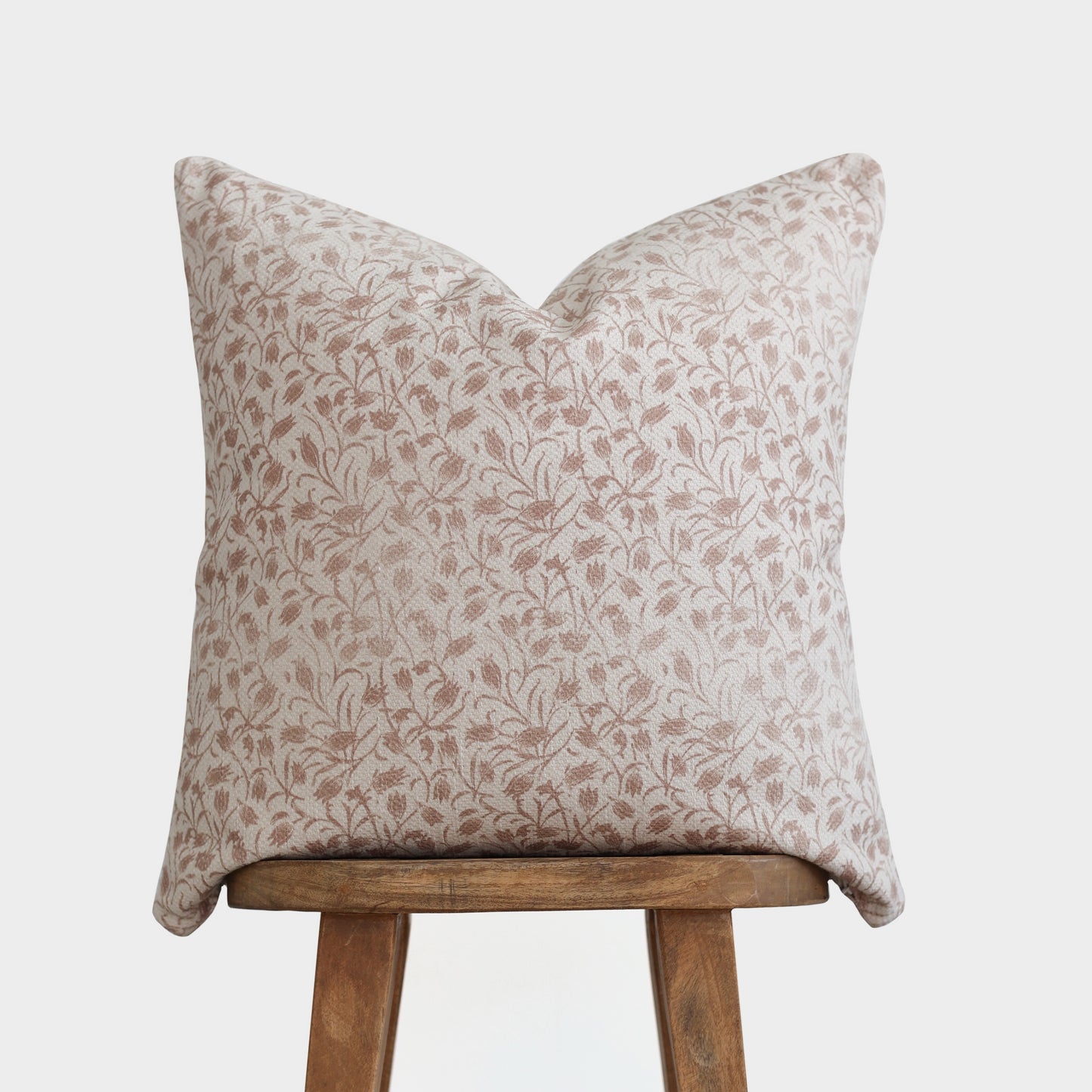 Beige and cream floral patterned throw pillow with thick weave fabric displayed on wooden stool.