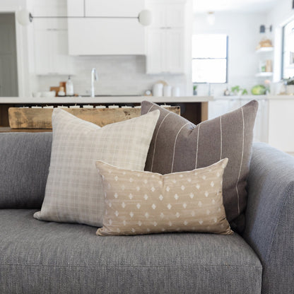 Taupe and white diamond patterned pillow displayed on a gray sofa with coordinating neutral pillows.