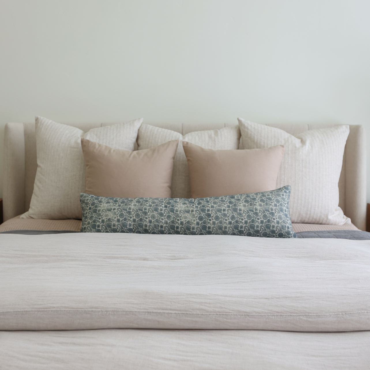 Blue patterned lumbar pillow displayed among neutral and cream-colored pillows on a bed.