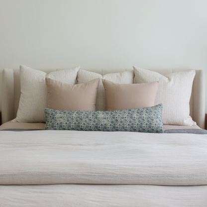 Blue patterned lumbar pillow displayed among neutral and cream-colored pillows on a bed.