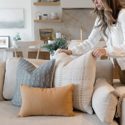 Sage green leaf-patterned pillow displayed on a beige sofa with coordinating pillows in a living room setting.