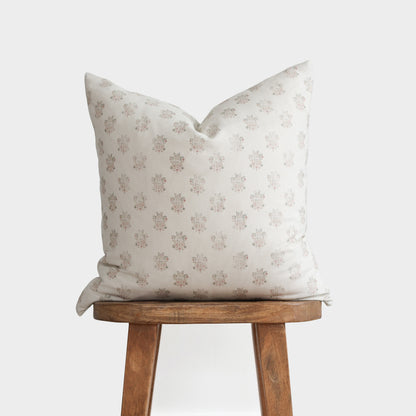 Cream pillow with small floral pattern in taupe and pink tones, displayed on wooden stool.