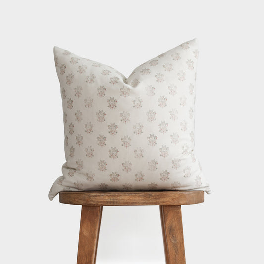 Cream pillow with small floral pattern in taupe and pink tones, displayed on wooden stool.