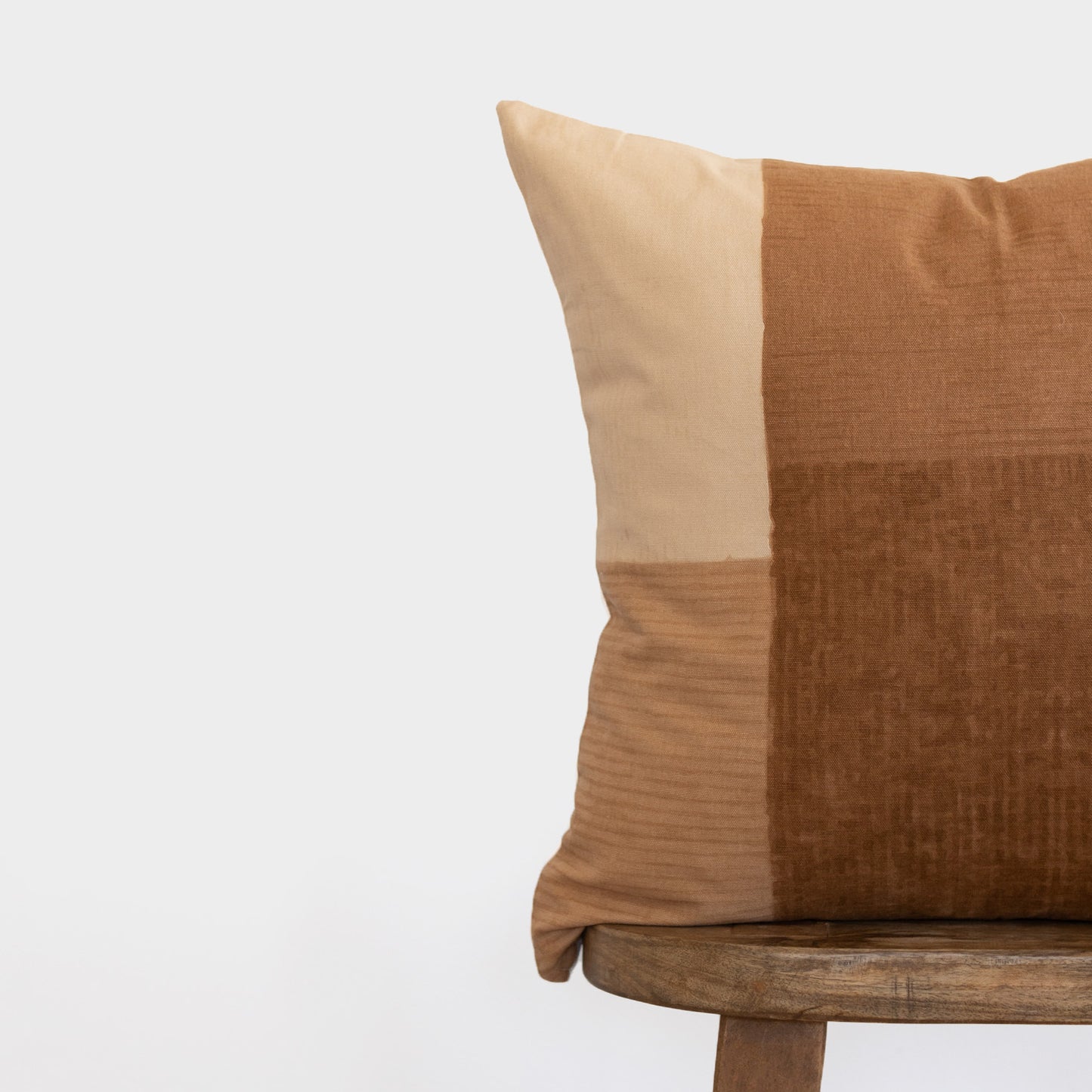 Tierra pillow with color-blocked design in cream and tan tones on wooden chair.