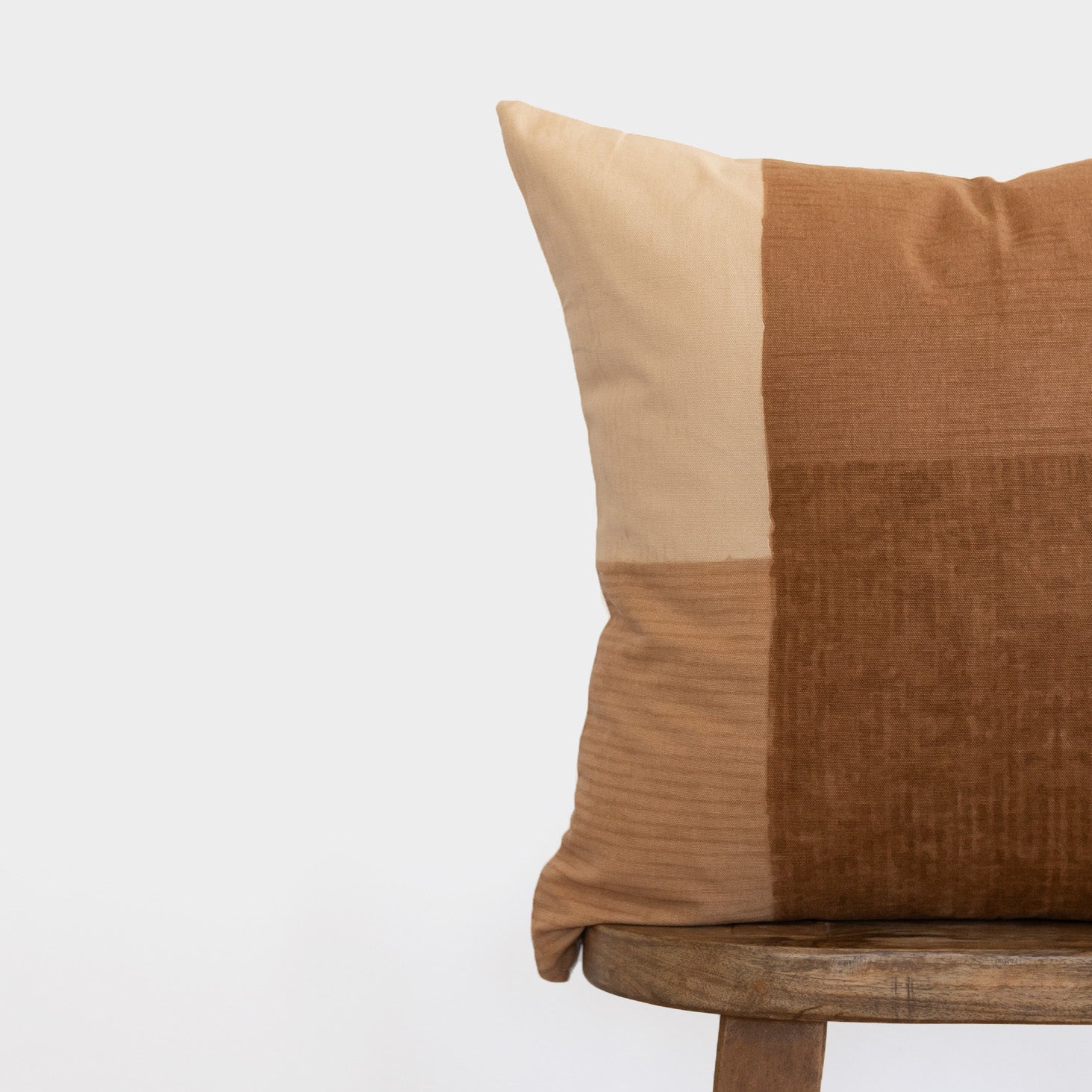 Tierra pillow with color-blocked design in cream and tan tones on wooden chair.